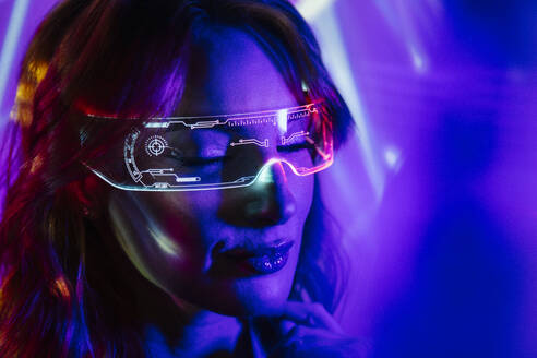 Porträt einer jungen Frau mit geschlossenen Augen, Brille und Freizeitkleidung mit leuchtendem Neonlicht im Gesicht und einer futuristischen Brille - ADSF32389