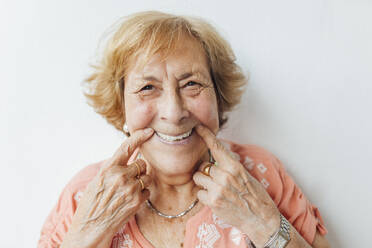 Ältere Frau hält Wangen vor einer weißen Wand - EGHF00262