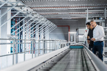 Businessman and manager looking at equipment on conveyor belt in factory - DIGF17003