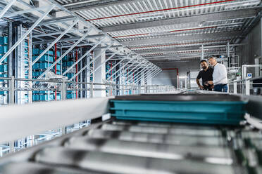 Manager examining equipment on conveyor belt with coworker in warehouse - DIGF17005