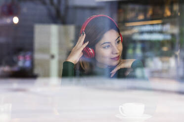 Frau hört Musik über Kopfhörer am Fenster eines Cafés - PNAF02606