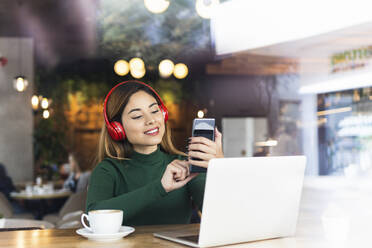 Lächelnde Geschäftsfrau mit Laptop und Smartphone in einem Café - PNAF02624