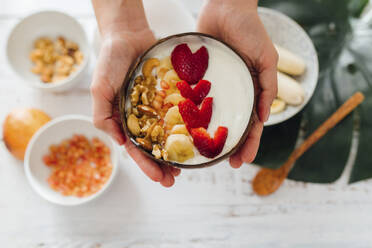 Woman holding bowl of yogurt and fruits over table - EGHF00275