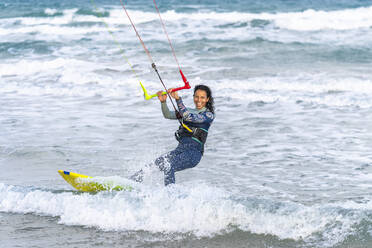 Fröhliche Frau beim Surfen mit Kiteboard auf dem Wasser - DLTSF02455