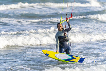 Glückliche Frau mit Kiteboard, die den Griff des Drachenfallschirms im Wasser hält - DLTSF02460