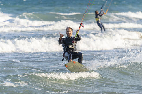 Lächelnder Mann beim Kiteboarden mit Frau im Hintergrund im Urlaub - DLTSF02463