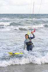 Lächelnde Frau mit Kiteboard, die den Griff des Kite-Fallschirms im Wasser hält - DLTSF02464