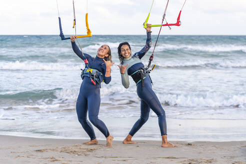 Cheerful friends gesturing and kitesurfing at beach - DLTSF02467