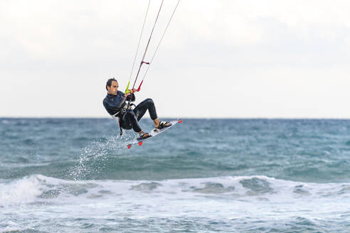Mann spritzt im Wasser und fährt Kiteboarding auf dem Meer - DLTSF02470