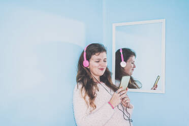 Woman wearing headphones using mobile phone by mirror - SVCF00066
