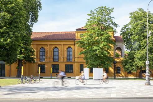 Germany, Bavaria, Munich, People riding bicycles in front of Lenbachhaus museum - MAMF01974