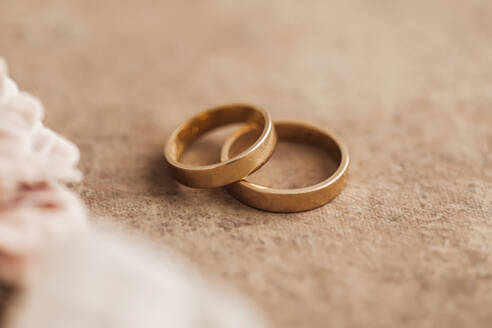 Studio shot of pair of golden wedding rings lying against brown background - FLMF00731