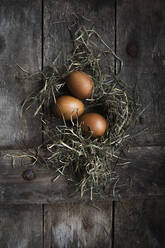 Studioaufnahme von drei Hühnereiern, die mit Heu auf einer Holzfläche liegen - EVGF03950