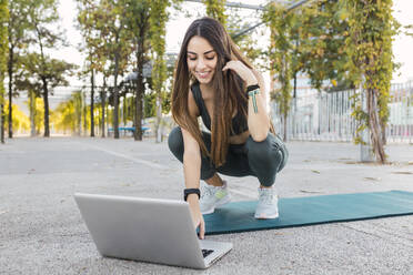 Smiling athlete using laptop in park - JRVF02148