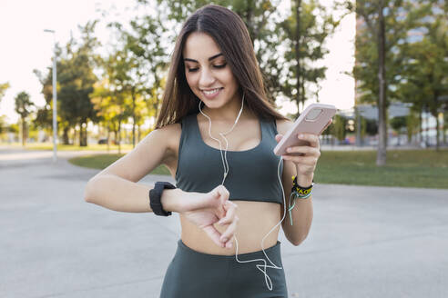 Schöne Sportlerin mit Mobiltelefon, die die Zeit im Park beobachtet - JRVF02153