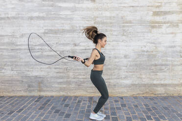 Sportswoman with rope jumping by wall - JRVF02158