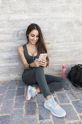 Lächelnde Sportlerin, die auf dem Gehweg ein Mobiltelefon benutzt - JRVF02159