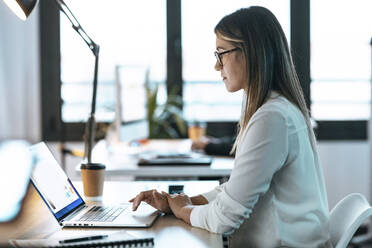 Businesswoman using laptop at desk in office - JSRF01737