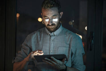 Businessman wearing eyeglasses working on digital tablet in office - JSRF01742