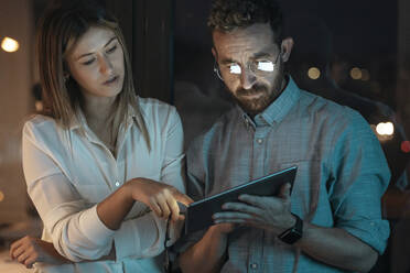 Businesswoman explaining strategy over tablet PC to colleague in office at late night - JSRF01745