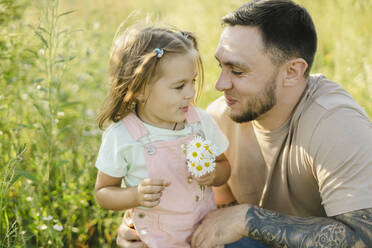 Smiling father looking at daughter holding daisies - SEAF00194