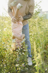 Father holding daughter upside down by daisies in meadow - SEAF00199