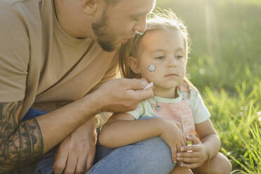 Girl with tattoo on face sitting with father by plants - SEAF00206