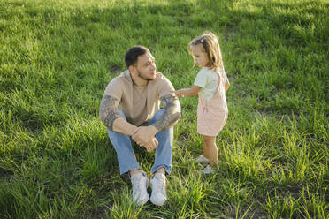 Girl standing by father sitting on grass - SEAF00208