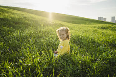 Nettes Mädchen sitzt im Gras auf einer Wiese an einem sonnigen Tag - SEAF00215