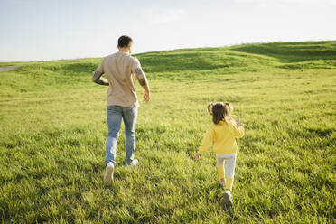 Vater und Tochter laufen über eine Wiesenlandschaft - SEAF00217