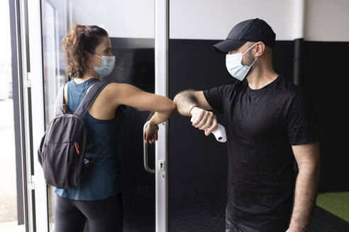 Friends wearing protective face mask greeting in gym - JPTF00923