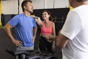 Lächelnde Frau lehnt an der Schulter eines Mannes im Fitnessstudio - JPTF00926