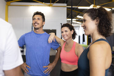 Lächelnde Freunde betrachten einen Sportler im Fitnessstudio - JPTF00928