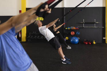 Athleten lehnen sich nach hinten und ziehen Riemen im Fitnessstudio - JPTF00934