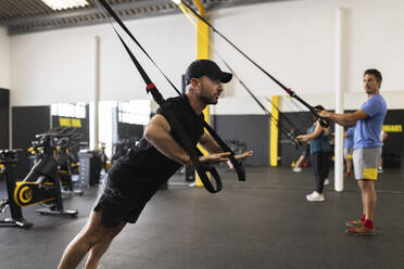 Trainer mit Riemen, der Sportler in der Turnhalle anleitet - JPTF00935