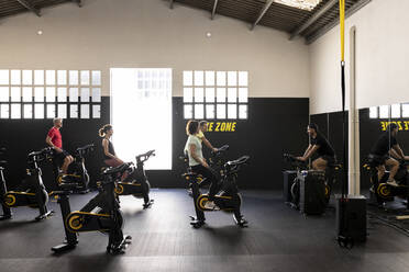 Coach instructing athletes cycling in gym - JPTF00947