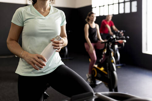 Sportlerin mit Wasserflasche auf dem Heimtrainer im Fitnessstudio - JPTF00948