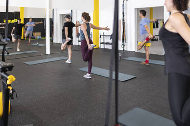 Athleten dehnen sich auf einem Bein vor einem Spiegel im Fitnessstudio - JPTF00970