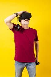 Man watching augmented reality through headset against yellow background - GPF00258