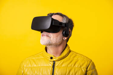 Man with hair stubble watching augmented reality through headset against yellow background - GPF00262