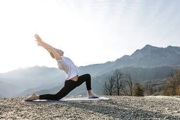 Man with arms raised doing Anjaneyasana with mountain view - OMIF00204