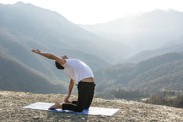 Man practicing Ustrasana on exercise mat - OMIF00205