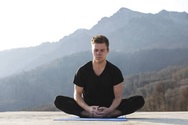 Konzentrierter Mann meditiert im Lotussitz auf Übungsmatte - OMIF00211