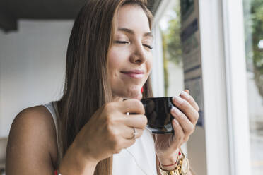 Frau mit geschlossenen Augen riecht Kaffee aus einer Tasse im Café - DSIF00581