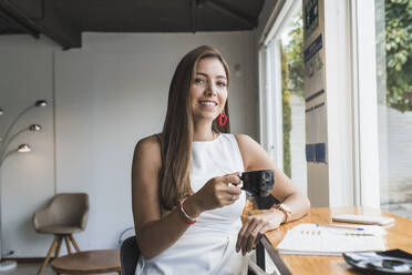 Schöne Frau hält Kaffeetasse lächelnd im Café - DSIF00583