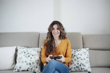 Frau mit Joystick, die ein Videospiel spielt, sitzt zu Hause auf dem Sofa - EBBF04932