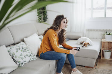 Frau sitzt auf dem Sofa und spielt ein Videospiel zu Hause - EBBF04934