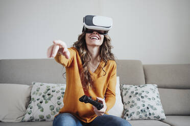 Frau mit Joystickgesten, die zu Hause ein Virtual-Reality-Headset trägt - EBBF04939