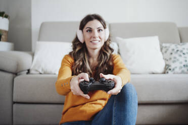 Young woman wearing headphones playing video game at home - EBBF04942