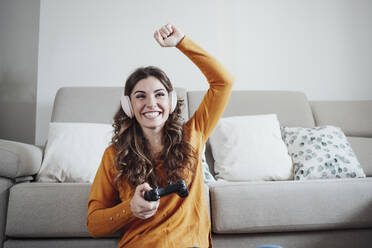 Happy woman with hand raised playing video game at home - EBBF04943